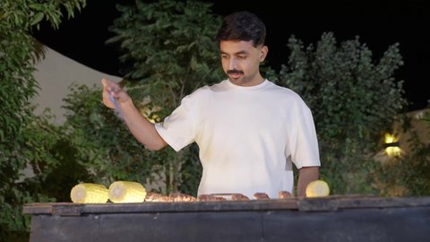 فعاليات وأنشطة مسلية، التعاون والمشاركة في تحضير الطعام،  تحضير الشواء في التجمعات، تصوير مقرب لولد عربي خليجي سعودي يرتدي الزي الكاجوال ويقوم بعملية الشواء تقليب اللحم على الموقد التأكد من طهيه جيدا، التنزه والتسلية في شاليه سياحي راقي وقت العطلة