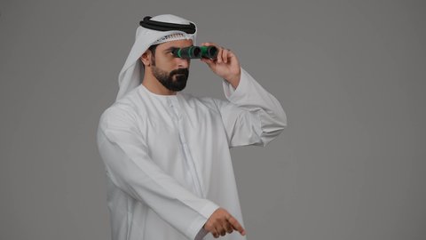 حب المغامرة والاستكشاف، رؤية الاشياء البعيدة عبر التلسكوب، نظرة ورؤية مستقبلية، بورتريه لرجل عربي خليجي إماراتي يرتدي الكندورة والغترة ينظر من خلال المنظار ثنائي العينين، خلفية رمادية