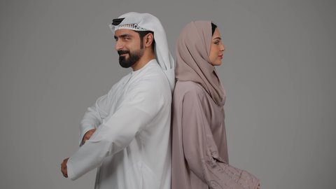 Standing straight with crossed hands, expressions and gestures of self-confidence, portrait of an Arab Gulf Emirati couple wearing Emirati dress looking at the camera, concept of elegance and attention to one's appearance, white background