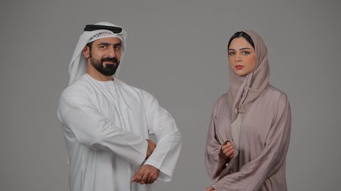 تعابير وايماءات الثقة بالنفس، الوقوف باستقامة وأيدي متقاطعة، بورتريه  لزوجين عربيين خليجيين إماراتيين يرتديان الزي الاماراتي ينظران إلى الكاميرا، مفهوم الأناقة والاهتمام بالمظهر الخارجي، خلفية بيضاء