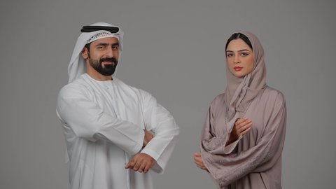الوقوف باستقامة وأيدي متقاطعة، تعابير وايماءات الثقة بالنفس، بورتريه  لزوجين عربيين خليجيين إماراتيين يرتديان الزي الاماراتي ينظران إلى الكاميرا، مفهوم الأناقة والاهتمام بالمظهر الخارجي، خلفية بيضاء