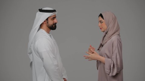 دفاع المراه عن نفسها، رجل إماراتي يرتدي الغترة والكندورة يقوم بضرب وتعنيف زوجته بالعقال، شجار بين الزوجين، مشاكل عائلية وصراع اسري، ازمة في العلاقات الاسرية، بورتريه لزوجين عربيين خليجيين اماراتيين يتجادلان مع بعضهما بإيماءات الغضب، خلفية بيضاء