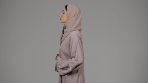 مفهوم الأنوثة والجمال، الأناقة والاهتمام بالكظهر الخارجي، بورتريه لامرأة عربية خليجية اماراتية ترتدي العباءة والحجاب تقف بأيدي متقاطعة، امراة سعودية تنظر إلى الكاميرا بإيماءات الثقة بالنفس، خلفية بيضاء