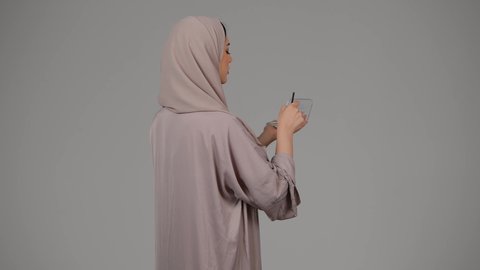 التسويق لمنتجات التجميل، مفهوم الانوثه والاهتمام بالمظهر الخارجي، سيدة اماراتية تستخدم أدوات تجميل نسائيه عصريه، مكياج وميكاب تتوريال، بورتريه من الجانب لامرأة عربيه سعودية خليجيه ترتدي العباءة والحجاب تحمل بيدها فرشاة توريد الخدود، خلفية بيضاء