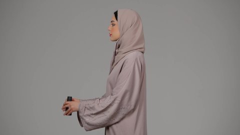 التخطيط المستقبلي للأهداف و الطموحات، بورتريه لامرأة عربية خليجية اماراتية محجبة ترتدي العباءة والحجاب تنظر من خلال منظار, حب الاستكشاف والمغامرة، شابة سعودية تقوم برؤية الاشياء البعيدة عبر التلسكوب، خلفية رمادية