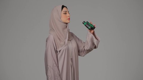 الإشارة بإصبع السبابة إلى شيء ما، التخطيط المستقبلي للأهداف و الطموحات، بورتريه لامرأة عربية خليجية اماراتية محجبة ترتدي العباءة تنظر من خلال منظار, حب الاستكشاف والمغامرة، شابة سعودية تقوم برؤية الاشياء البعيدة عبر التلسكوب، خلفية رمادية