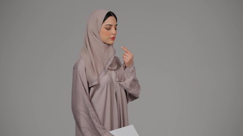قراءة الملاحظات والمعلومات، متابعة الخطط والمشاريع ، أوراق خاصة بالعمل, تدوين المهام اليومية، بورتريه لامراة عربيه خليجيه اماراتيه محجبه ترتدي العباءة تحمل بيديها أوراق بيضاء، شابه سعوديه تقوم بالبحث العلمي، ايماءات الجدية والثقة بالنفس، خلفية رمادية