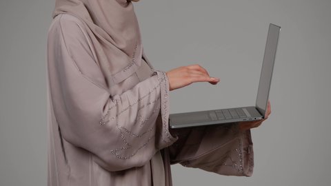إتقان الكتابة على لوحة المفاتيح، إدارة شؤون الأعمال، تصفح الإنترنت وإستخدام اجهزة تقنية حديثة، بورتريه من الجانب لشابة عربية خليجية اماراتية تقوم بالعمل على الحاسوب المحمول، العمل لتحقيق الاهداف، سيده سعودية تستخدم الحاسوب المحمول لإنجاز المهام، خلفية رمادية