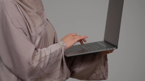 إدارة شؤون الأعمال وتنظيمها، تصفح الإنترنت وإستخدام اجهزة تقنية حديثة، بورتريه من الجانب لشابة عربية خليجية اماراتية تقوم بالعمل على الحاسوب المحمول، العمل لتحقيق الاهداف والاستراتيجيات، سيده سعودية تستخدم الحاسوب المحمول لإنجاز المهام، خلفية رمادية