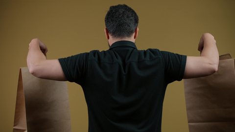 المتعة في التسوق، الاستفادة من مواسم العروض والحسومات والتصفيات، المشتريات التجارية والهدايا, التبضع وأخذ الاحتياجات اللازمة, تصوير من الخلف لرجل عربي خليجي اماراتي يرتدي الكندورة و يمسك بيده أكياس ورقية، خلفية صفراء