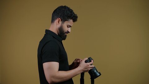 تصوير لشاب عربي خليجي اماراتي يرتدي الزي الكاجوال يمسك بيده كاميرا فوتوغرافية،مصور محترف يقوم بالتقاط صور تذكارية, اتقان التصوير الفوتوغرافي باستخدام كاميرات رقمية عالية الدقة, ممارسة هواية التصوير بتعابير السرور, خلفية صفراء