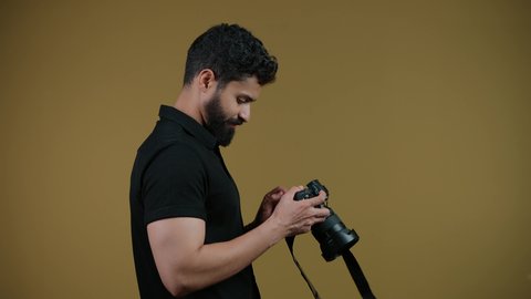 مصور محترف يقوم بالتقاط صور تذكارية, اتقان التصوير الفوتوغرافي باستخدام كاميرات رقمية عالية الدقة, ممارسة هواية التصوير بتعابير السرور, تصوير لشاب عربي خليجي اماراتي يرتدي الزي الكاجوال يمسك بيده كاميرا فوتوغرافية، خلفية صفراء