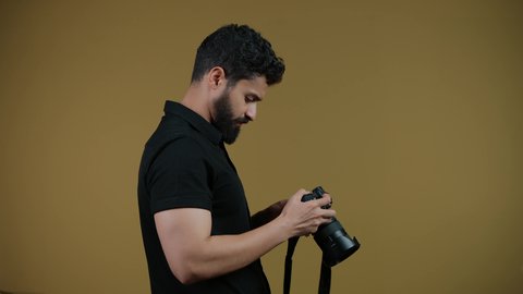 اتقان التصوير الفوتوغرافي باستخدام كاميرات رقمية عالية الدقة, مصور محترف يقوم بالتقاط صور تذكارية, ممارسة هواية التصوير بتعابير السرور, تصوير لشاب عربي خليجي اماراتي يرتدي الزي الكاجوال يمسك بيده كاميرا فوتوغرافية، خلفية صفراء