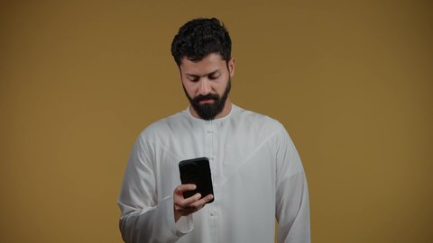 Looking with gestures of happiness, using modern and advanced technology, making phone calls, a picture of an Emirati Gulf Arab man wearing a kandura holding a mobile phone in his hand, yellow background