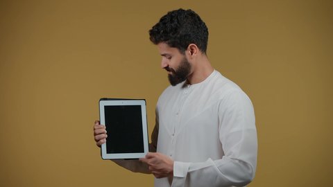 Blank black screen on tablet, looking at camera with happy gestures, using modern and advanced technology, depicting an Emirati Gulf Arab man wearing a kandura holding a tablet, yellow background