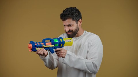 Expressions of enthusiasm and joy, having a good time playing water games in the summer, a picture of an Emirati Gulf Arab young man wearing a kandura holding a plastic water gun playing with gestures of pleasure and happiness, the concept of entertainment and amusement, yellow background