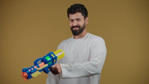 Having fun with water games in the summer, a picture of an Emirati Gulf Arab young man wearing a kandura holding a plastic water gun playing with gestures of pleasure and happiness, expressions of enthusiasm and joy, the concept of entertainment and amusement, yellow background