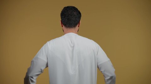 النظر إلى الكاميرا بتعابير السرور، الاستفادة من الخصومات والتصفيات، المشتريات التجارية والهدايا, التبضع وأخذ الاحتياجات اللازمة, مواسم العروض والتخفيضات, تصوير من الخلف لرجل عربي خليجي اماراتي يرتدي الكندورة و يمسك بيده أكياس ورقية، خلفية صفراء