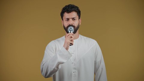 تصوير لشاب عربي خليجي اماراتي يرتدي الكندورة يقوم بالغناء باستخدام الميكروفون بتعابير الحماس, الاندماج مع الأغنية، مواهب غنائية فنية،تسجيل مقطع صوتي غنائي، خلفيه صفراء