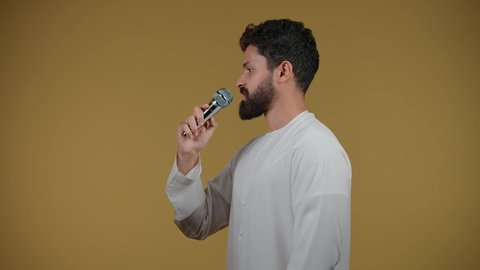 Merging with the song, artistic singing talents, recording a singing audio clip, filming a young Emirati Gulf Arab man wearing a kandura singing using a microphone with enthusiastic expressions, yellow background
