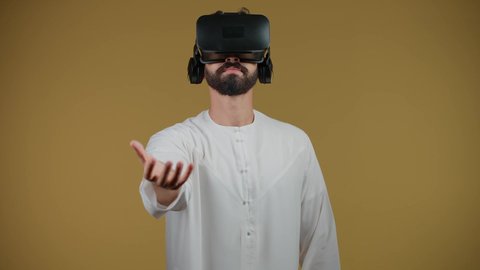 مشاهدة الأفلام ومحاكاة العالم الخيالي,  التفاعل والاندماج مع ألعاب الواقع الافتراضي,تصوير لشاب عربي اماراتي خليجي يرتدي الكندورة ونظارة في آر ثلاثية الأبعاد, رجل اماراتي يرفع قبضة يده لمحاولة إمساك شيء ما، خلفية صفراء