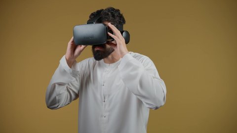Interacting and immersing in virtual reality games, watching movies and simulating the imaginary world, a picture of a young Emirati Gulf Arab man wearing a kandura and 3D VR glasses, an Emirati man raising his fist to try to grab something, yellow background