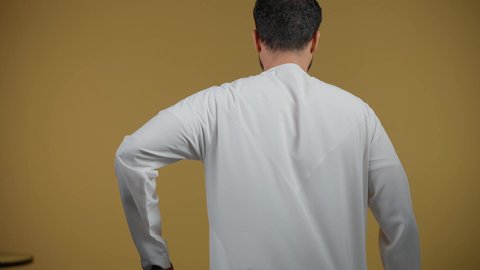 مفهوم السياحة والسفر، القيام بجولات ترفيهية في إجازة الصيف, تصوير من الخلف لشاب عربي خليجي اماراتي يرتدي الكندورة يحمل حقيبة السفر, الاستعداد لقضاء رحلة صيفية ممتعة، خلفية صفراء