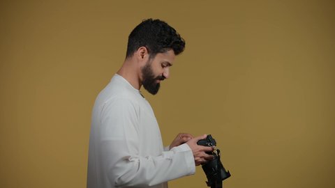 ممارسة هواية التصوير بتعابير السرور, اتقان التصوير الفوتوغرافي باستخدام كاميرات رقمية عالية الدقة, مصور محترف يقوم بالتقاط صور تذكارية, تصوير لشاب عربي خليجي اماراتي يرتدي الكندورة يمسك بيده كاميرا فوتوغرافية، خلفية صفراء