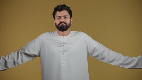 Mocking an ambiguous topic, wondering and asking about something, a picture of a young Emirati Gulf Arab man wearing a kandura looking at the camera and raising his hands up with gestures of ignorance, hesitation and lack of confidence, feeling confused and mysterious, yellow background