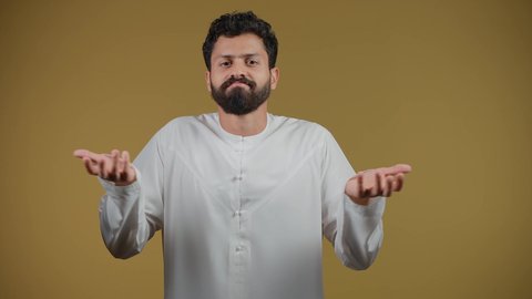 الاستغراب والاستفسار عن أمر ما،السخرية من موضوع مبهم،تصوير لشاب عربي خليجي إماراتي يرتدي الكندورة ينظر إلى الكاميرا ويرفع يديه نحو الأعلى بإيماءات عدم المعرفة, التردد وعدم الثقة، الشعور بالحيرة والغموض، خلفية صفراء