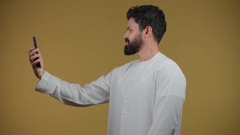 التواصل مع الأهل والأصدقاء, النظر إلى الكاميرا بإيماءات السؤال والاستفسار عن شيء ما، متابعة آخر الأخبار والمستجدات حول العالم, تصوير لشاب عربي خليجي اماراتي يرتدي الكندورة يجري مكالمة هاتفية، خلفية صفراء