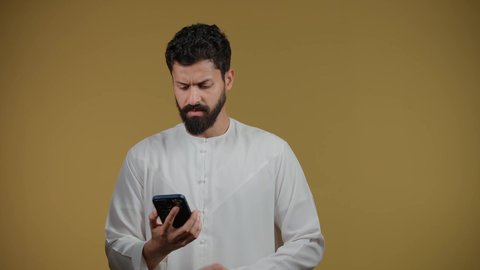 إيماءات السؤال والاستفسار عن شيء ما، التواصل مع الأهل والأصدقاء, متابعة آخر الأخبار والمستجدات حول العالم, تصوير لشاب عربي خليجي اماراتي يرتدي الكندورة يجري مكالمة هاتفية، خلفية صفراء
