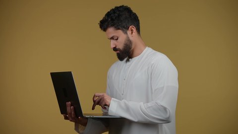 The concept of diligence and completion of required tasks, browsing social networking sites, watching movies and series, a picture of an Emirati Gulf Arab young man wearing a kandura holding a laptop in his hand, making video calls via the laptop, yellow background