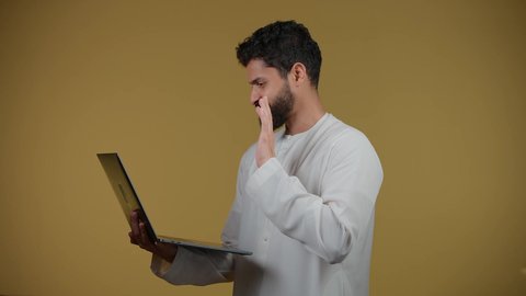 Watching movies and TV series, a picture of a young Emirati Gulf Arab man wearing a kandura holding a laptop, browsing social media, the concept of hard work and completing required tasks, making video calls via laptop, yellow background