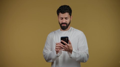 Following the latest news and developments around the world, communicating with family and friends, looking at the camera with gestures of question and inquiry about something, a picture of a young Emirati Gulf Arab man wearing a kandura making a phone call, yellow background