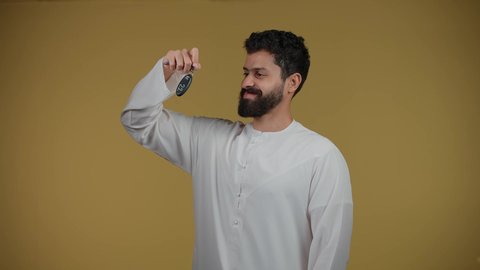 الحماس لامتلاك سيارة جديدة، خدمه صف السيارات بالمواقف الخاصه, استلام وتسليم المفاتيح، الحصول على رخصة القيادة،تصوير لشاب عربي خليجي اماراتي يرتدي الكندورة يمسك بيده مفتاح التحكم عن بعد,  خلفية صفراء