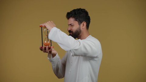 Realizing the value of precious moments in life, planning to achieve goals in the future, waiting for something impatiently, illustration of an Arab Gulf Emirati man wearing a kandura and holding an hourglass, observing the passage of time with gestures of seriousness and integration, yellow background