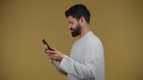 التواصل مع الأهل والأصدقاء, متابعة آخر الأخبار والمستجدات حول العالم, دمج التقنيات الحديثة والتكنولوجيا بالحياة العملية, تصوير لشاب عربي خليجي اماراتي يرتدي الكندورة يقوم باستخدام الهاتف المحمول، خلفية صفراء