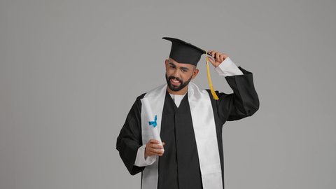 تصوير لشاب خريج عربي خليجي اماراتي يرتدي عباءة يرفع شهادة وقبعة التخرج، الاحتفال بإنهاء المرحلة الجامعية، الشعور بالفخر والفرح بالوصول لحلم التخرج, التعليم في الامارات العربية المتحدة، خلفية رماديه