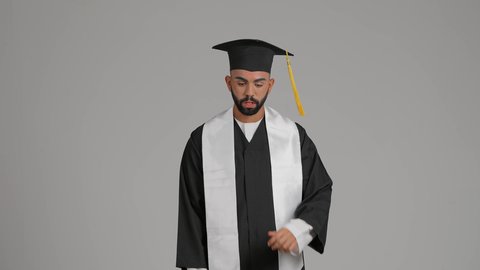 مفهوم الاجتهاد والتفوق، تعابير التفكير والحيرة، مناسبة النجاح في الجامعة، الاحتفال بإنهاء الدراسة الجامعية، الوصول لحلم النجاح، جودة التعليم في الامارات، تصوير لشاب خريج عربي خليجي اماراتي مبتسم يرتدي عباءة وقبعة التخرج  ، خلفية رماديه