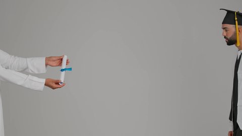 الوصول لحلم النجاح، تعابير السعادة والسرور، جودة التعليم في الامارات،مناسبة النجاح في الجامعة، الاحتفال بإنهاء الدراسة الجامعية، مفهوم الاجتهاد والتفوق، تصوير لشاب خريج عربي خليجي اماراتي مبتسم يرتدي عباءة وقبعة التخرج يأخذ الشهادة بايماءات الفخر ، خلفية رماديه