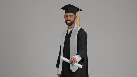 Expressions of happiness and joy, the occasion of university success, the quality of education in the UAE, achieving the dream of success, celebrating the completion of university studies, the concept of diligence and excellence, a photograph of a smiling young Emirati Gulf Arab graduate wearing a graduation gown and cap, holding a diploma, gray background.
