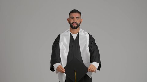 التعليم في الامارات العربية المتحدة، الشعور بالفخر والفرح بالوصول لحلم التخرج, تصوير لشاب خريج عربي خليجي اماراتي يرتدي عباءة يرفع قبعة التخرج، الاحتفال بإنهاء المرحلة الجامعية، خلفية رماديه