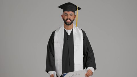 الاحتفال بإنهاء الدراسة الجامعية، مفهوم الاجتهاد والتفوق، تعابير السعادة والسرور، مناسبة واحتفال جامعي، الوصول لحلم النجاح، تصوير لشاب خريج عربي خليجي اماراتي مبتسم يرتدي عباءة التخرج يمسك بيده الشهادة، خلفية رماديه