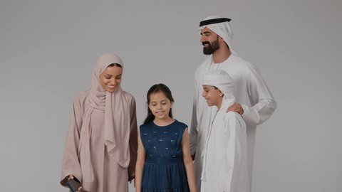 استخدام الأجهزة التقنية الحديثة، التقاط صور السيفلي التذكارية عبر الجوال، فرحة الأبناء بقضاء وقت ممتع مع الأهل، مشاعر الحب والحنان بين افراد الاسرة، أجواء أسرية مليئة بالمودة، بورتريه لام عربيه خليجيه اماراتية ترتدي العباءه الملونه تقوم بقضاء وقت ممتع برفقه اولادها و زوجها ، خلفية رمادية