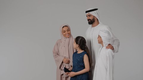 التقاط صور السيلفي التذكارية باستخدام الهاتف المحمول، فرحة الأبناء بقضاء وقت ممتع مع الأهل، مشاعر الحب والحنان بين افراد الاسرة، أجواء أسرية مليئة بالمودة، بورتريه لام عربيه خليجيه اماراتية ترتدي العباءه الملونه تقوم بقضاء وقت ممتع برفقه اولادها و زوجها ، خلفية رمادية