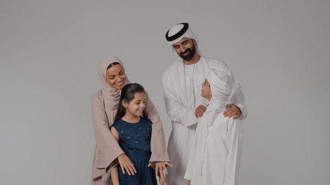 مشاعر الحب والحنان بين افراد الاسرة، الاستمتاع باللعب مع الأطفال بإيماءات السرور والسعاده، أجواء أسرية مليئة بالمودة، بورتريه لام عربيه خليجيه اماراتية ترتدي العباءه الملونه تقوم بقضاء وقت ممتع برفقه اولادها و زوجها ، خلفية رمادية