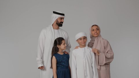 أجواء أسرية مليئة بالمودة، الاشارة إلى شيء ما بعيد والنظر إليه بإيماءات الاعجاب، المشي و التنزه مع الأطفال، بورتريه لام عربيه خليجيه اماراتية ترتدي العباءه الملونه تقوم بقضاء وقت ممتع برفقه اولادها و زوجها ، خلفية رمادية