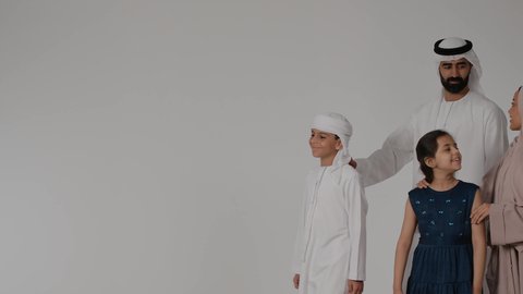 مفهوم الأسرة الإماراتية السعيدة، المشي و التنزه مع الأطفال، مفهوم الترابط الأسري، بورتريه لام عربيه خليجيه اماراتية ترتدي العباءه الملونه تقوم بقضاء وقت ممتع برفقه اولادها و زوجها بايماءات السعادة و السرور، خلفية رمادية