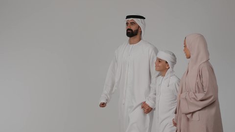 المشي و التنزه مع الأطفال، مفهوم الترابط الأسري، مشاركة الأوقات الممتعة مع الأبناء، بورتريه لام عربيه خليجيه اماراتية ترتدي العباءه الملونه تقوم بقضاء وقت ممتع برفقه زوجها و ابنها بايماءات السعادة و السرور، خلفية رمادية
